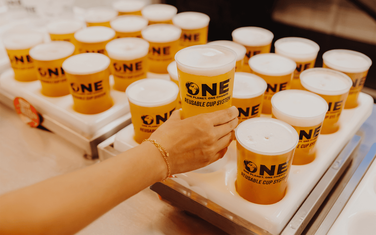 person picking up a drink that is in a One Cup, many more drinks in One Cups are in the background