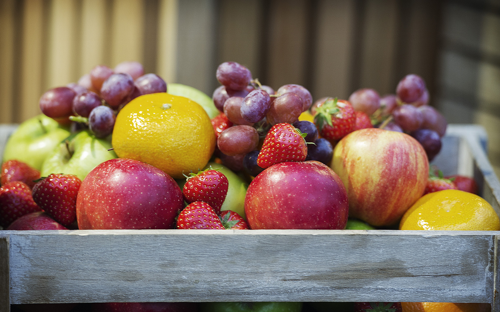 A wooden box full of fresh fruit like apples, grapes and strawberries. 
