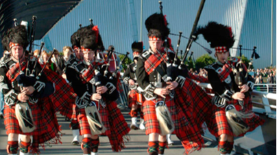 People dressed in kilts playing bagpipes on a bridge near the SEC.