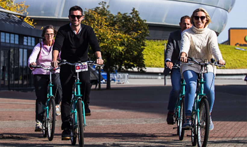 People cycling in front of the OVO Hydro.