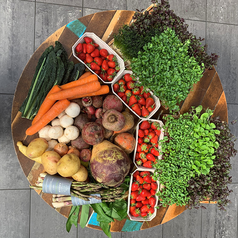 A wooden table covered in fresh fruit and vegetables like strawberries, potatoes, mushrooms and asparagus. 